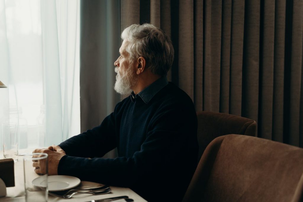 A man sitting quietly alone at a dining table, reflecting on healing after betrayal