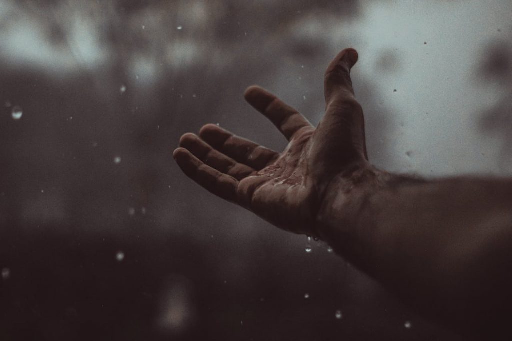 A hand reaching out into the rain, symbolising reaching out via a crisis support number when in crisis